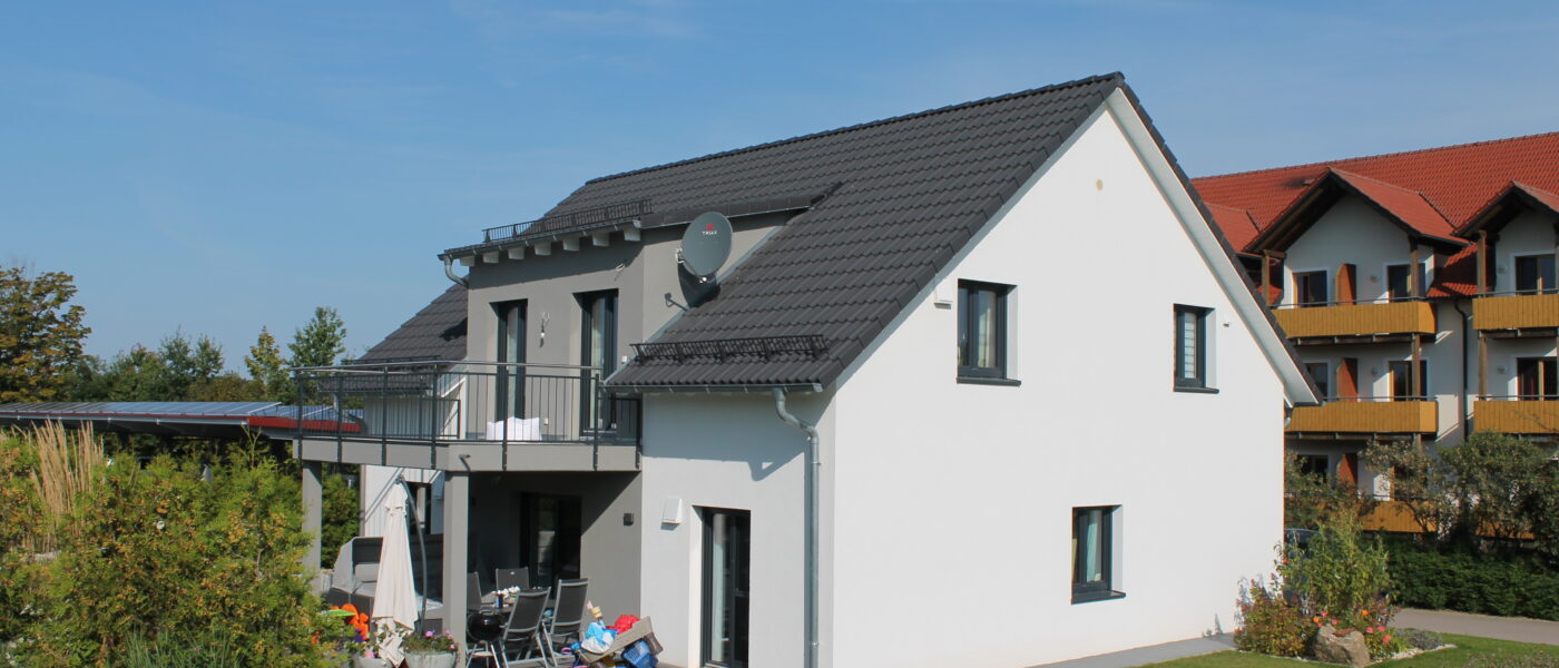 Dachformen fürs Haus – Ein Haus mit weißer Fassade, Satteldach und umliegenden Garten.