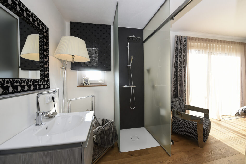 Luftfeuchtigkeit in Wohnräumen – Offenstehende Duschkabine in einem Badezimmer, das an ein Schlafzimmer grenzt.
