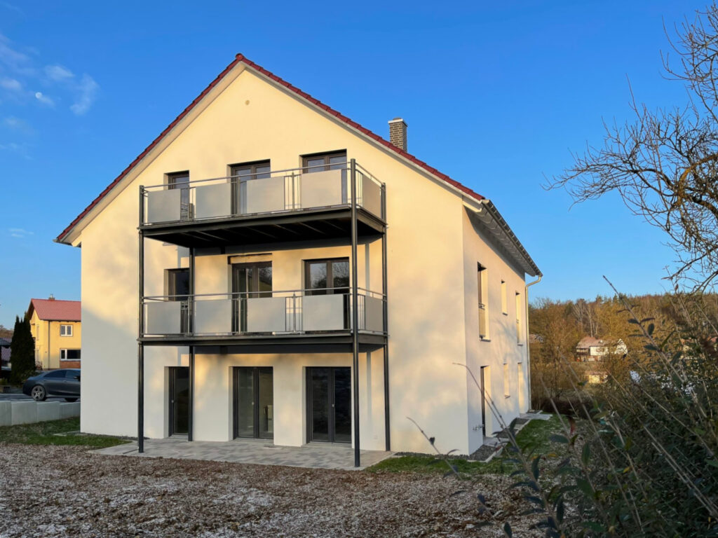 Mehrfamilienhaus als Kapitalanlage – Ein Mehrfamilienhaus von Rötzer mit weißer Fassade bei Sonnenuntergang.