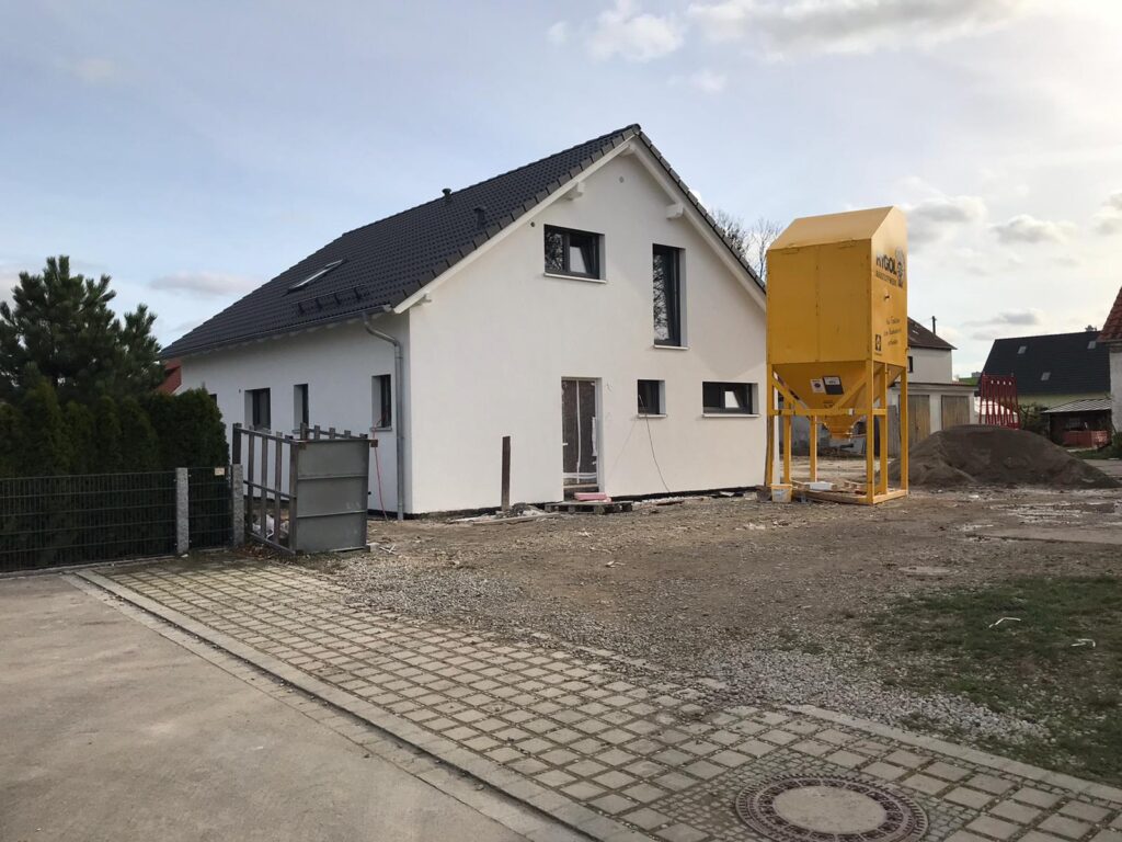 Grundbuch – Weißes Einfamilienhaus im Rohbau mit gelbem Bausilo auf einer Baustelle.